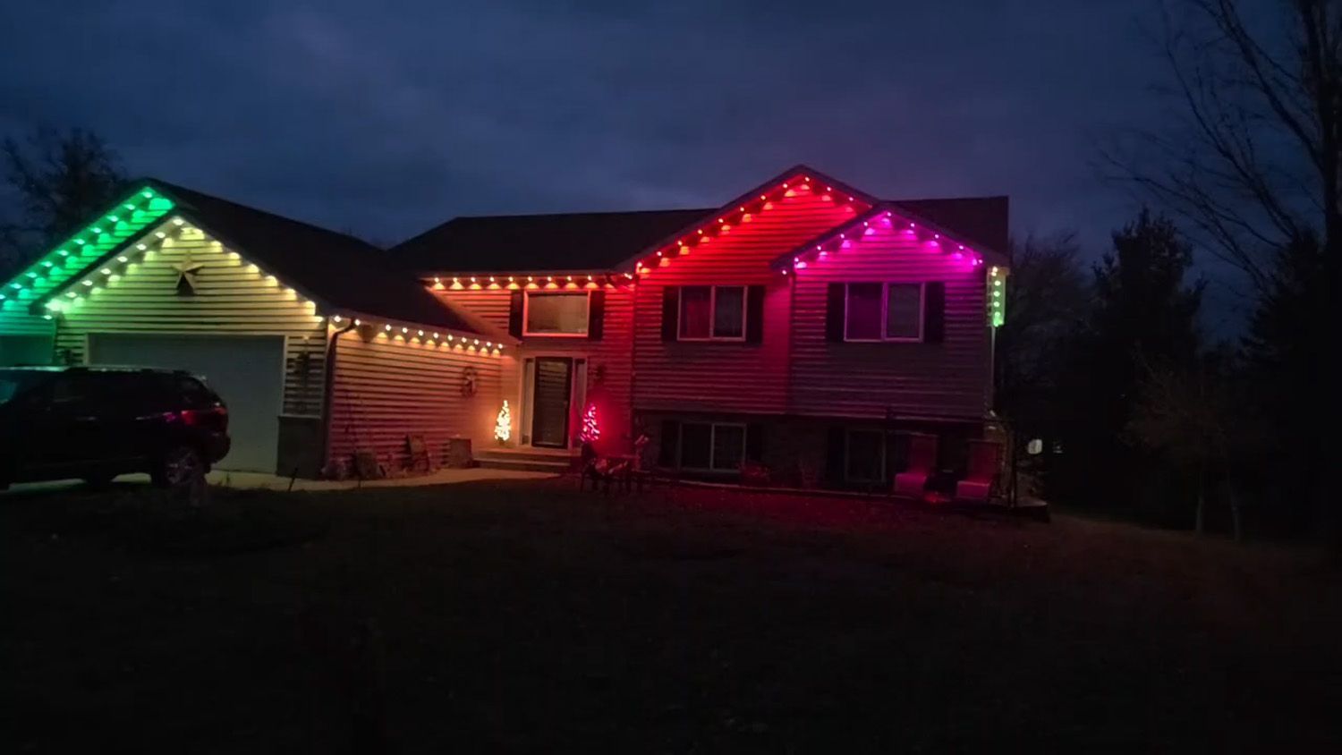 House at dusk outlined with green, red, and pink holiday lights, with a lit garage and dark yard