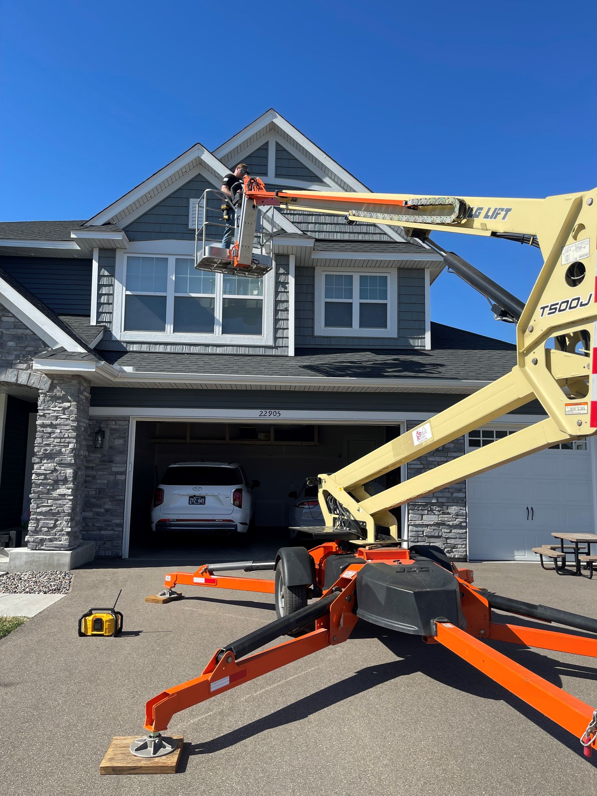 Lift truck and cherry picker working on a gray house roof under a clear blue sky