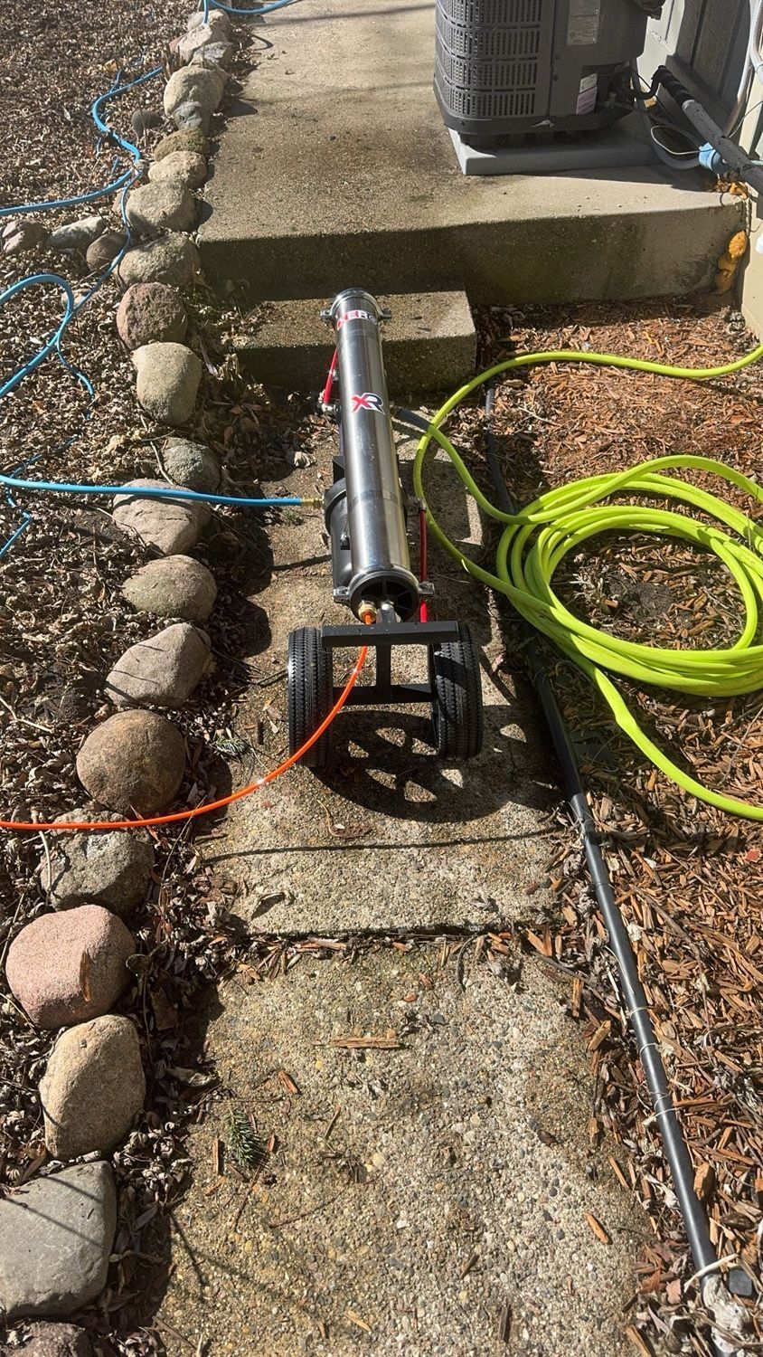 Pressure washer on a stone walkway beside a coiled green hose and a stone border