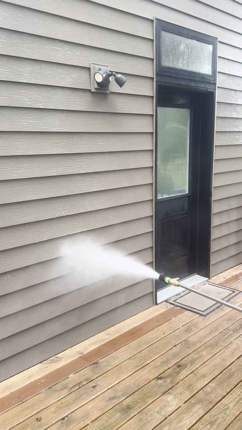 Water spraying from a hose near a black door on a house deck