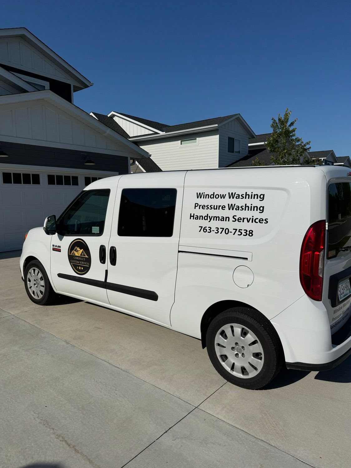 White service van with window-cleaning and pressure-washing business text parked in a driveway by a house