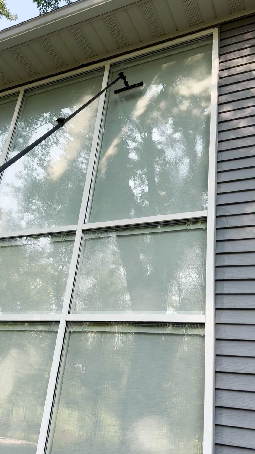 Exterior window with white curtains, dark brick siding, and a black window-cleaning tool attached to the glass.