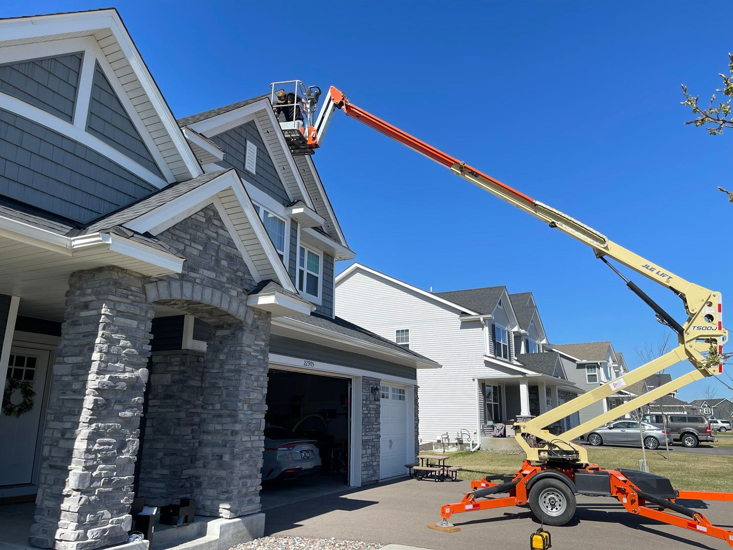 Worker in an orange lift repairing the roof of a gray suburban house on a sunny day