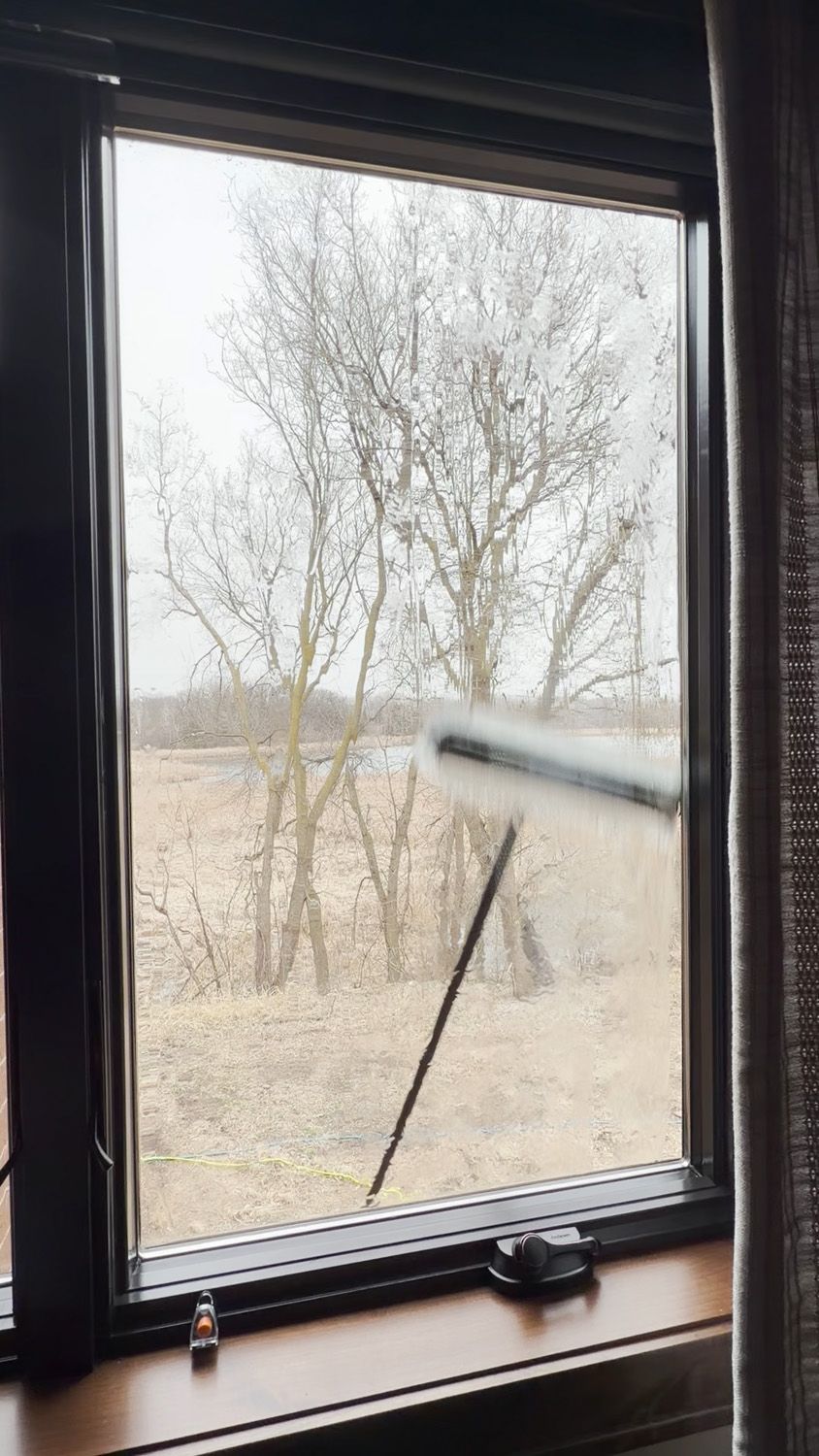 Rain-speckled window with a wiper and a view of leafless trees outside