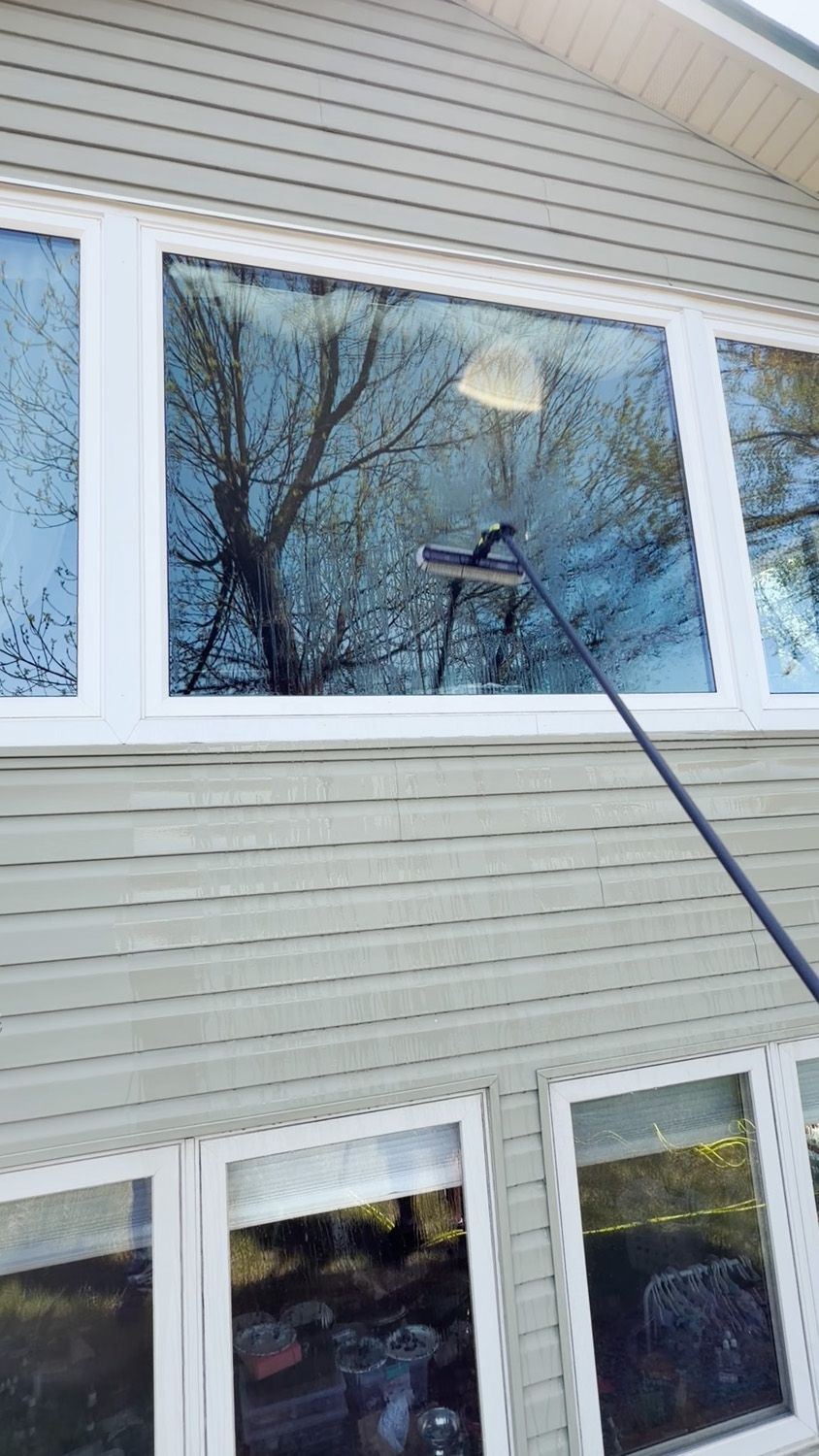 House exterior with beige siding and large windows being cleaned with a long-handled squeegee.
