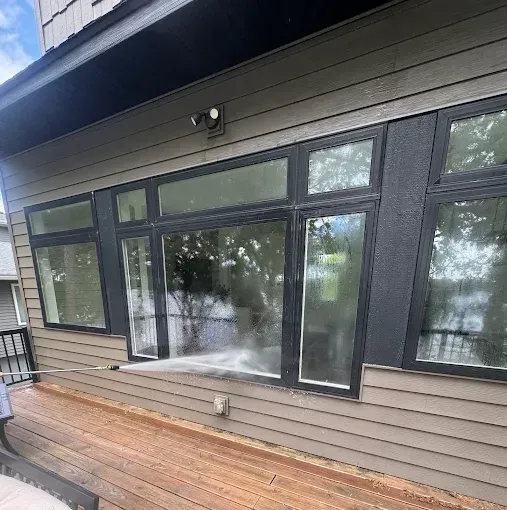 Exterior of a house with large black-framed windows and a wooden deck under the eaves