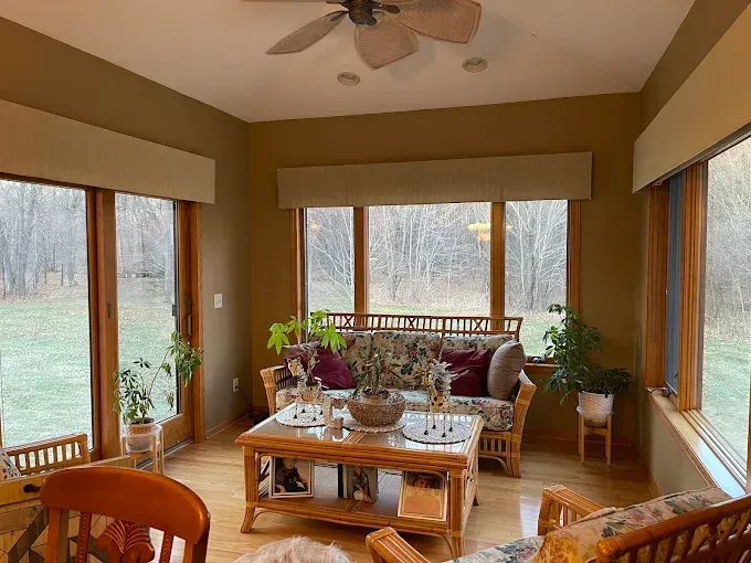 Sunroom with large windows, wicker seating, coffee table, and view of trees outside.