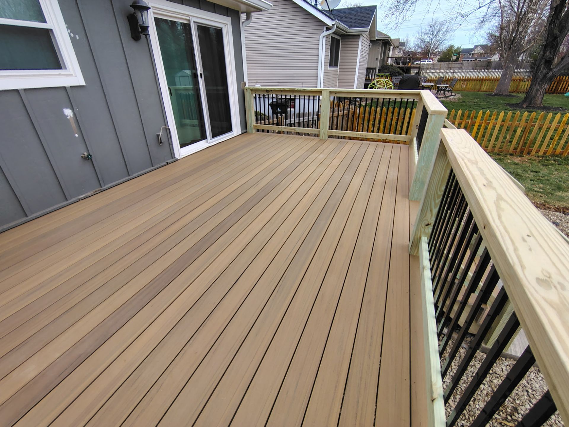 Spacious wooden backyard deck with railing beside a gray house, overlooking a fenced yard.