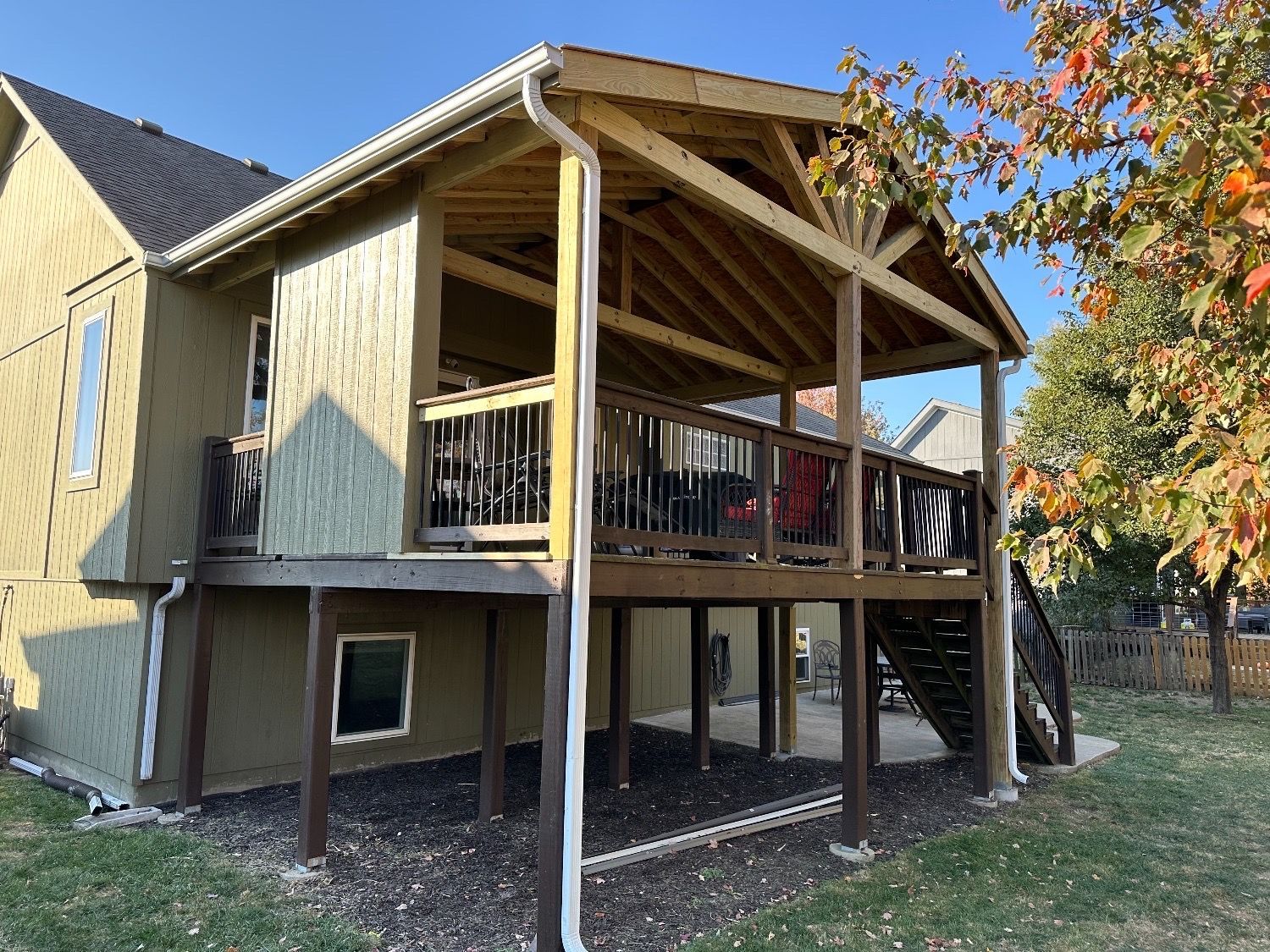 Raised wooden deck and covered porch on the back of a house, with stairs and autumn trees nearby