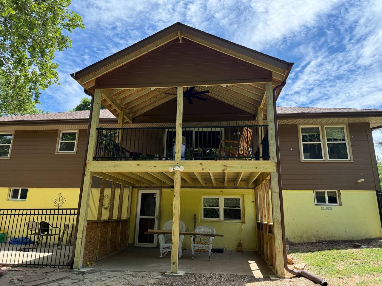Two-story house with a covered porch and wooden support beams under a blue sky