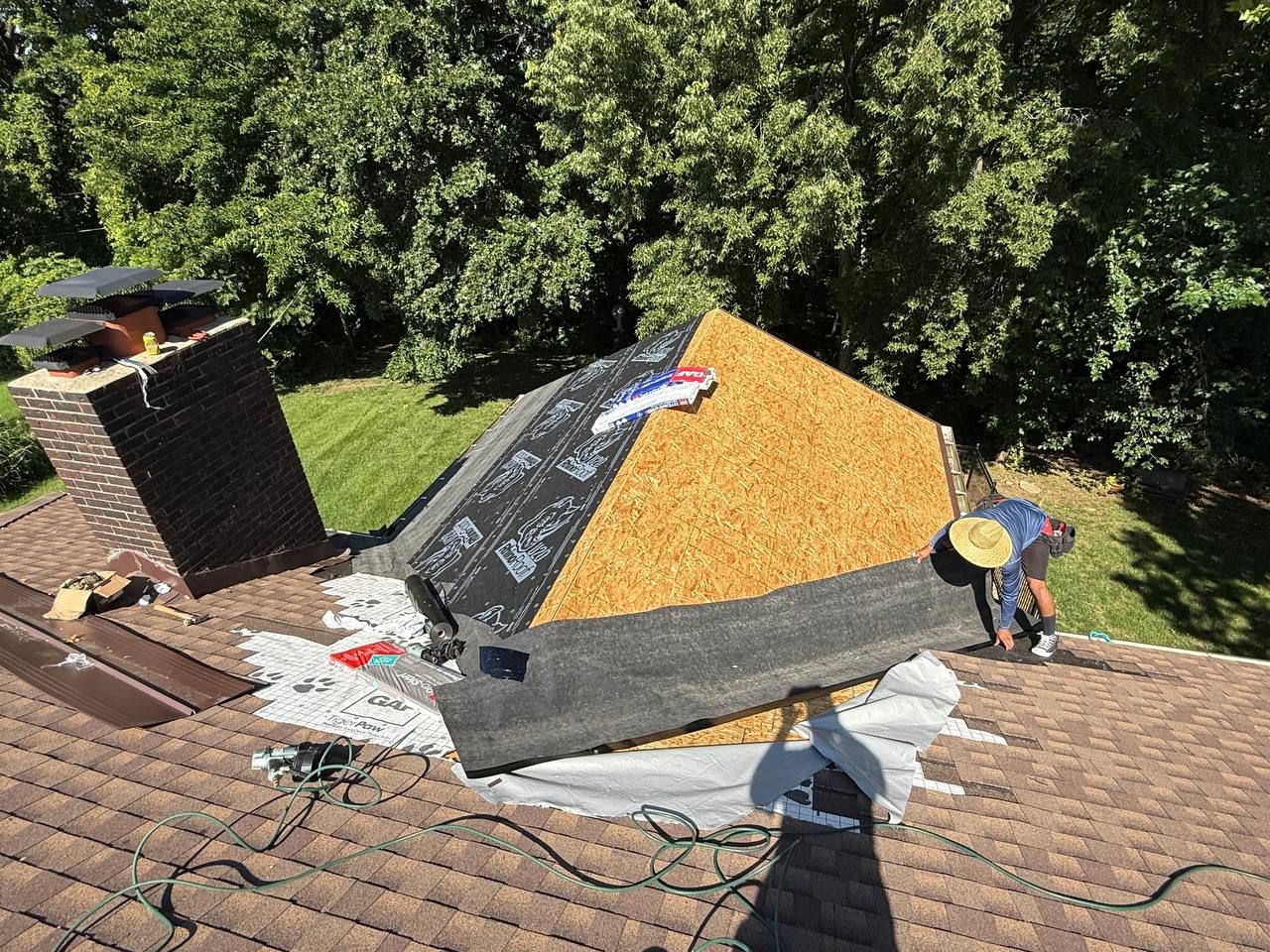 Roofers installing a new roof with black underlayment and orange shingles on a house surrounded by trees