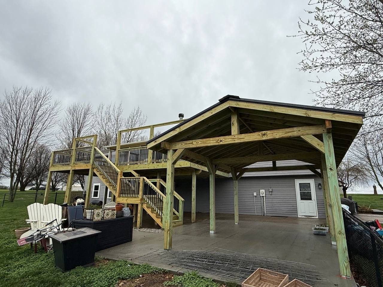 Wooden backyard pavilion with stairs and railing, open sides, and a shingled roof on a cloudy day