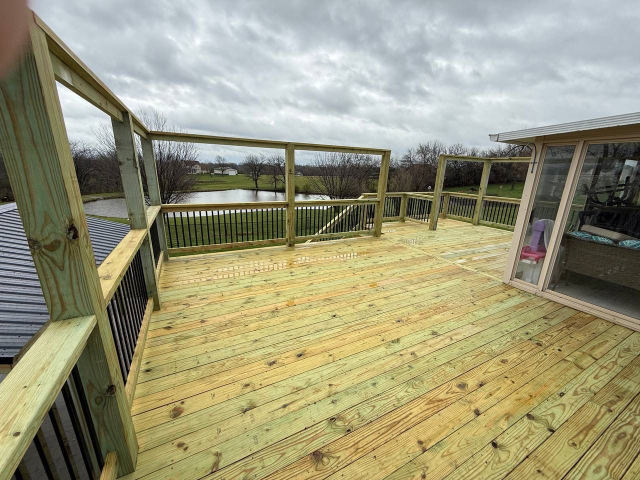 Wide wooden deck with railing overlooking a grassy yard under a cloudy sky