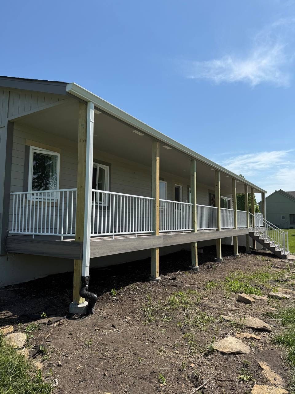 Long white porch on a raised house with railings, set on a dirt lot under a blue sky