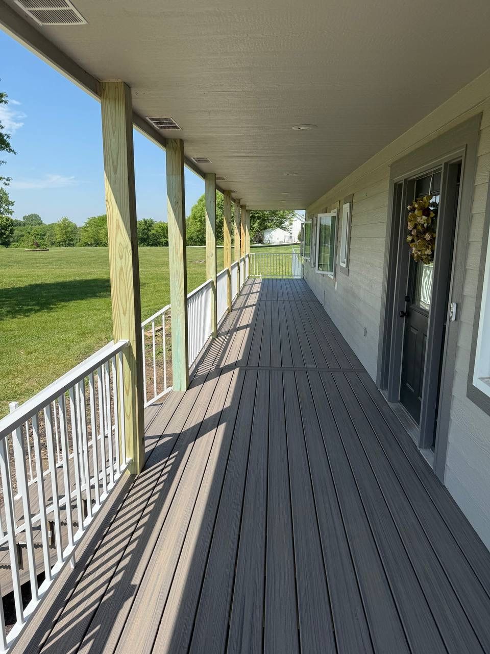 Covered porch with white railing and gray deck overlooking a grassy yard