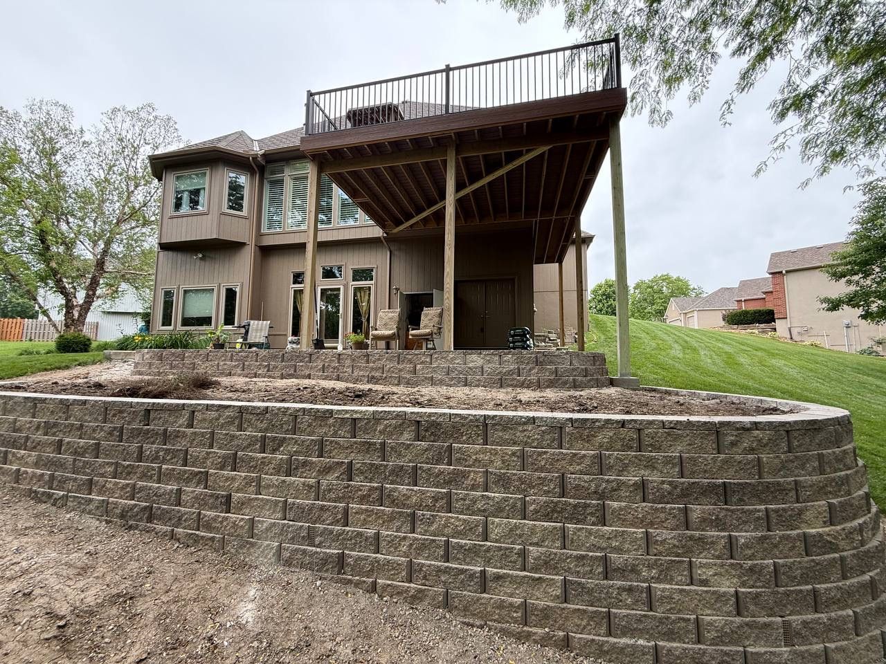 Stone house with elevated wooden deck and sloped retaining wall in a rural yard