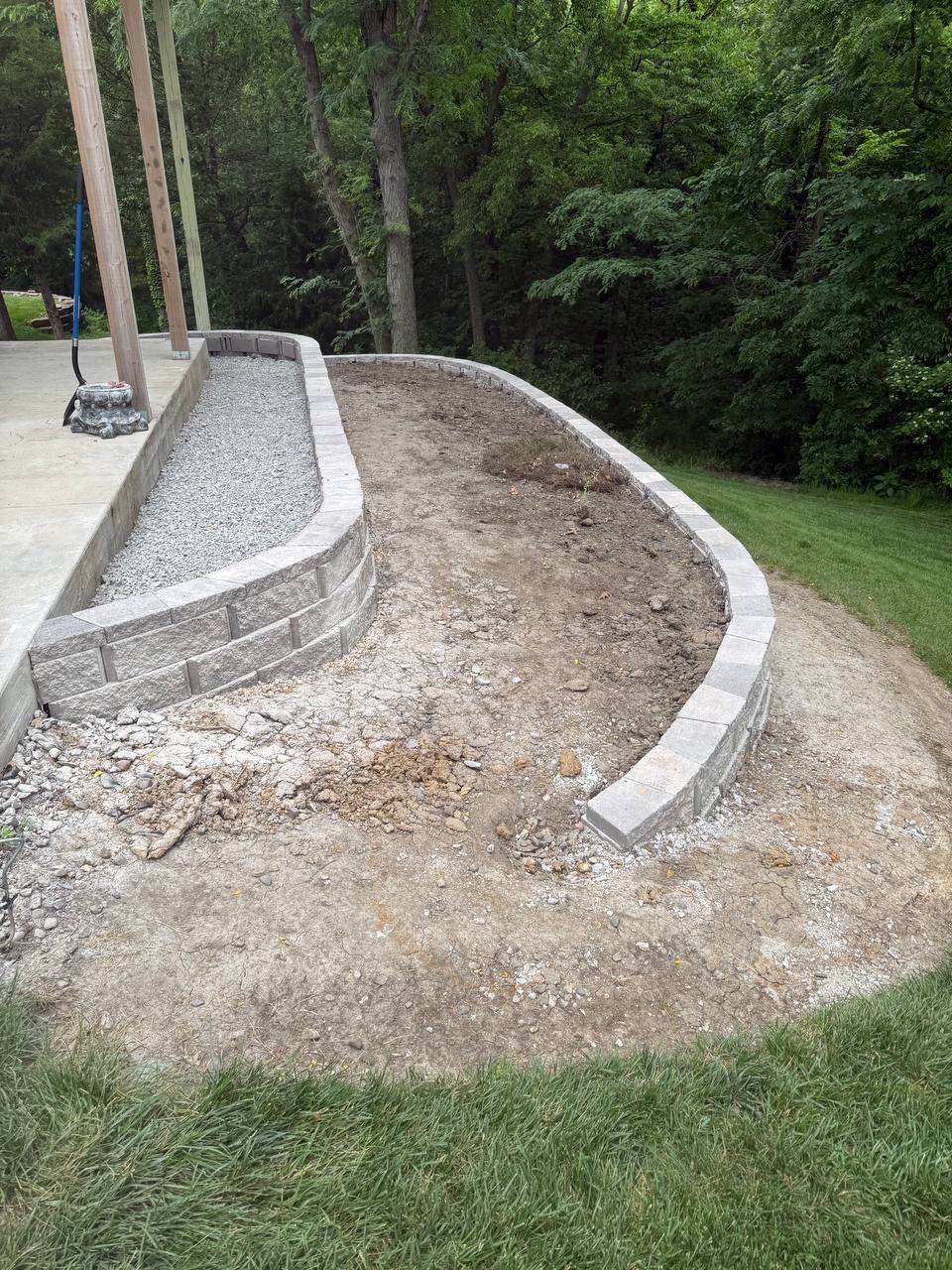 Curved concrete retaining wall around a gravel path in a wooded yard.