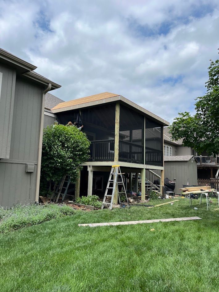 Backyard house exterior with raised deck, ladder, and cloudy sky
