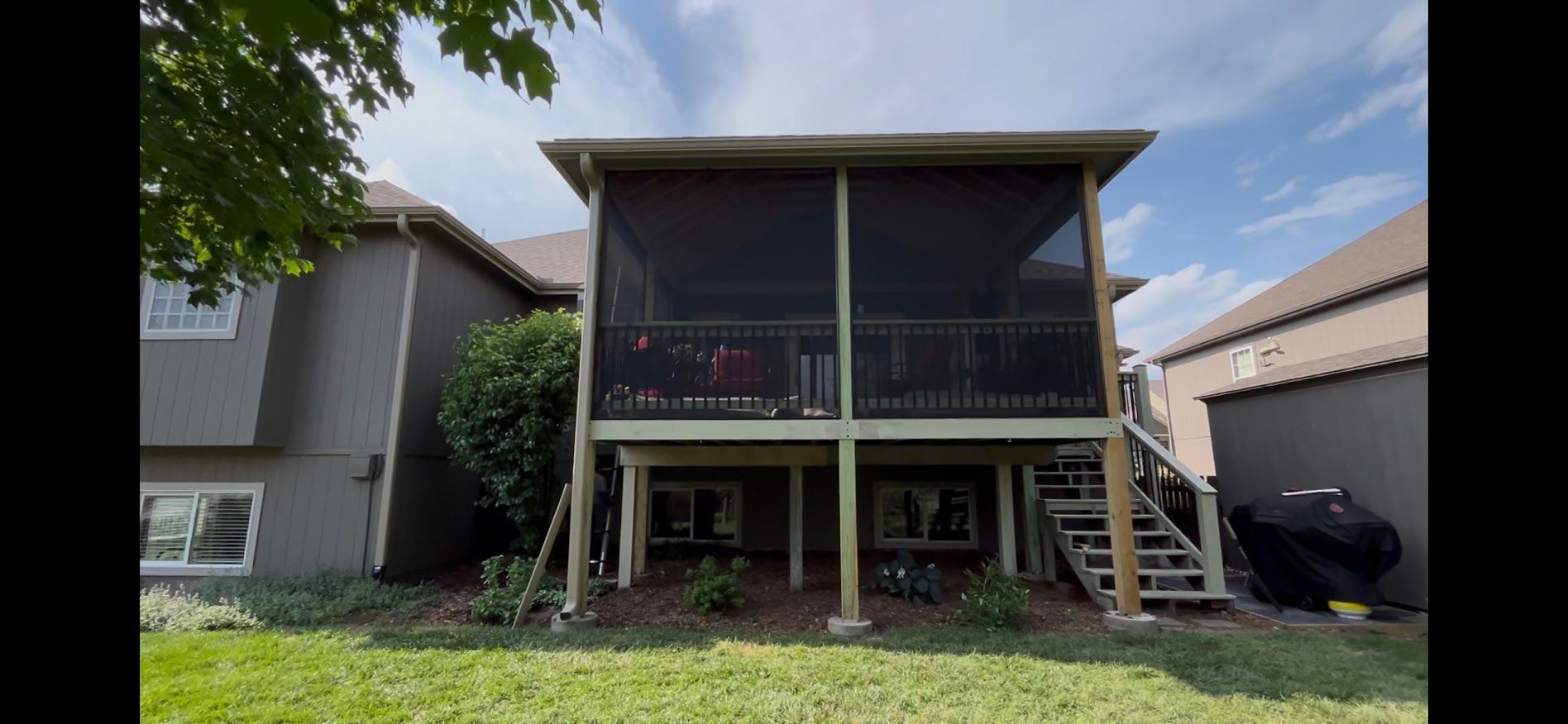 Two-story house with a covered front porch, dark siding, and a grassy yard under a blue sky