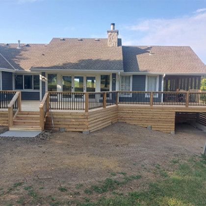 Back deck and stairs on a tan house with a stone chimney, viewed from the yard.