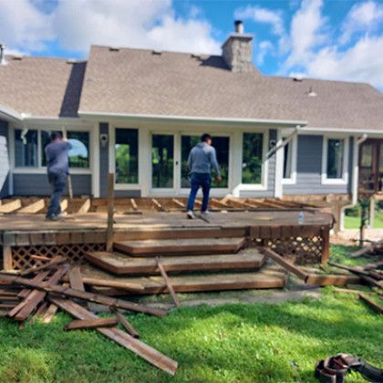 Two workers on a damaged wooden deck being rebuilt behind a house