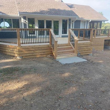 Wooden front porch with steps and railings on a house, overlooking a bare dirt yard.