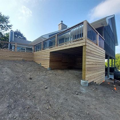 Wooden deck and staircase on a sloped dirt lot, with open under-deck storage area.