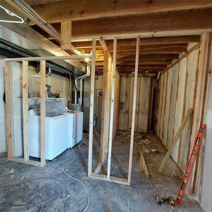 Basement renovation with exposed wooden framing, laundry appliances, and construction tools on a concrete floor
