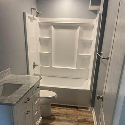 Small bathroom with white built-in shelving, a toilet, and a gray vanity with wood floor.