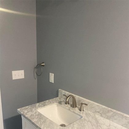 Gray bathroom vanity with white sink, marble countertop, and chrome faucet against a gray wall