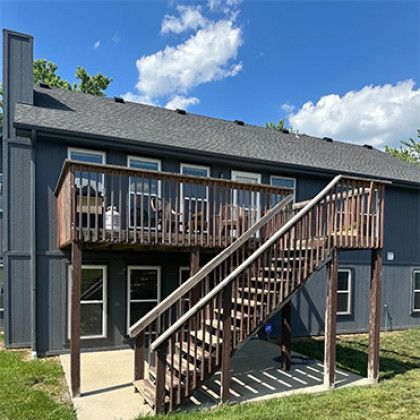 Backyard deck with wooden stairs on a dark blue house under a sunny sky