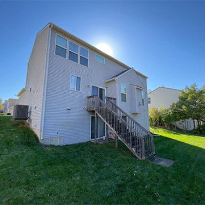White two-story house with an exterior staircase and grassy yard in bright sunlight