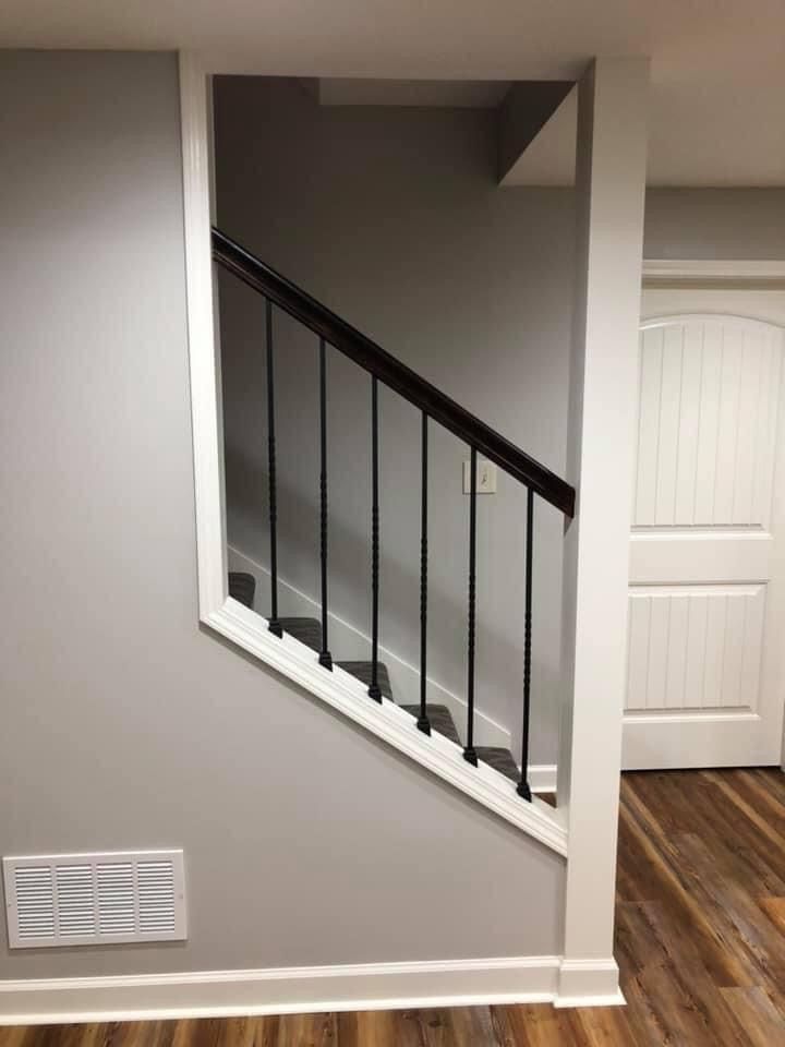 Staircase with black railing in a gray hallway beside a white door and vent cover