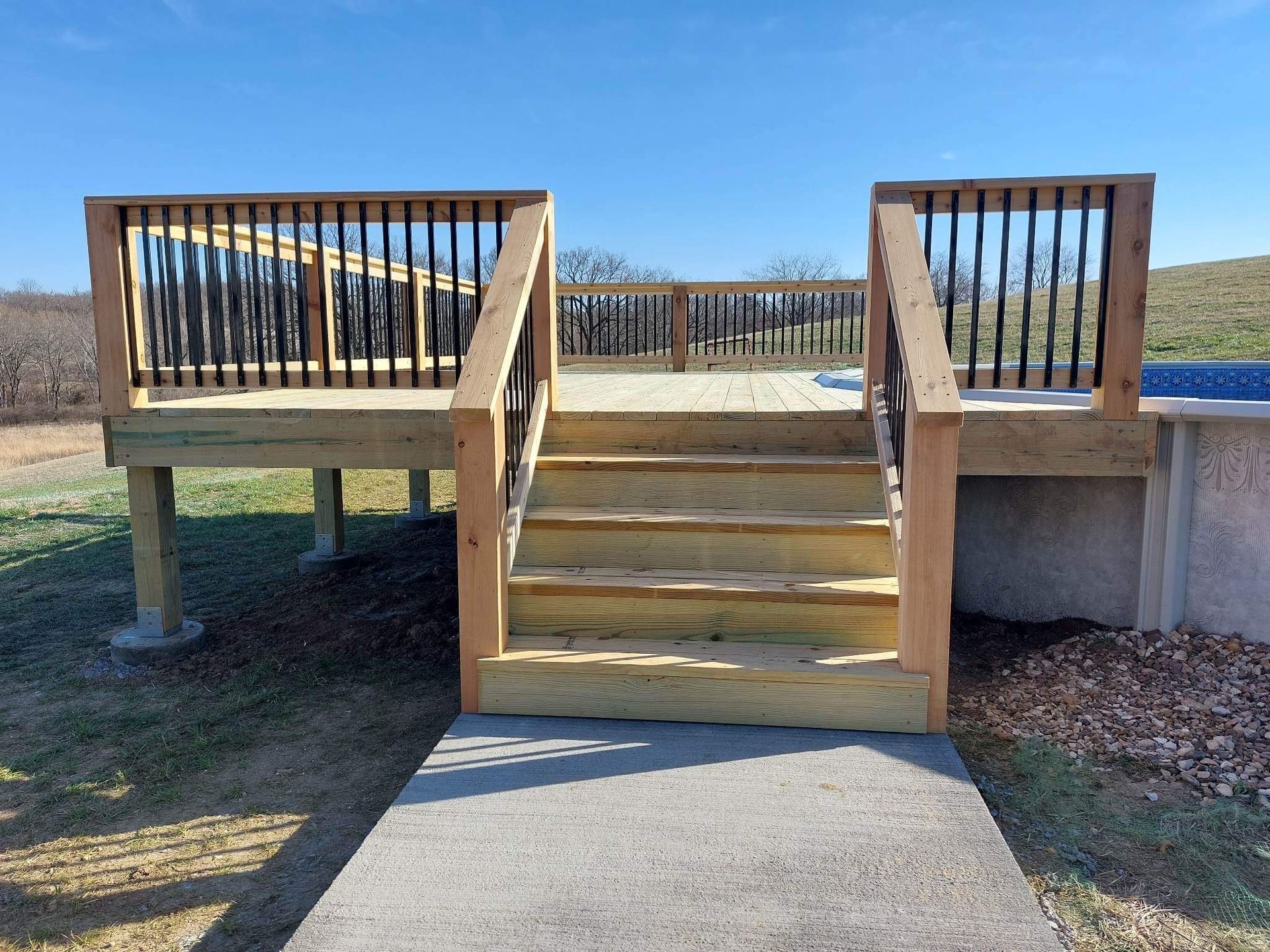 Wooden ramp with stairs leading to a raised deck, with railings and a concrete path in front.