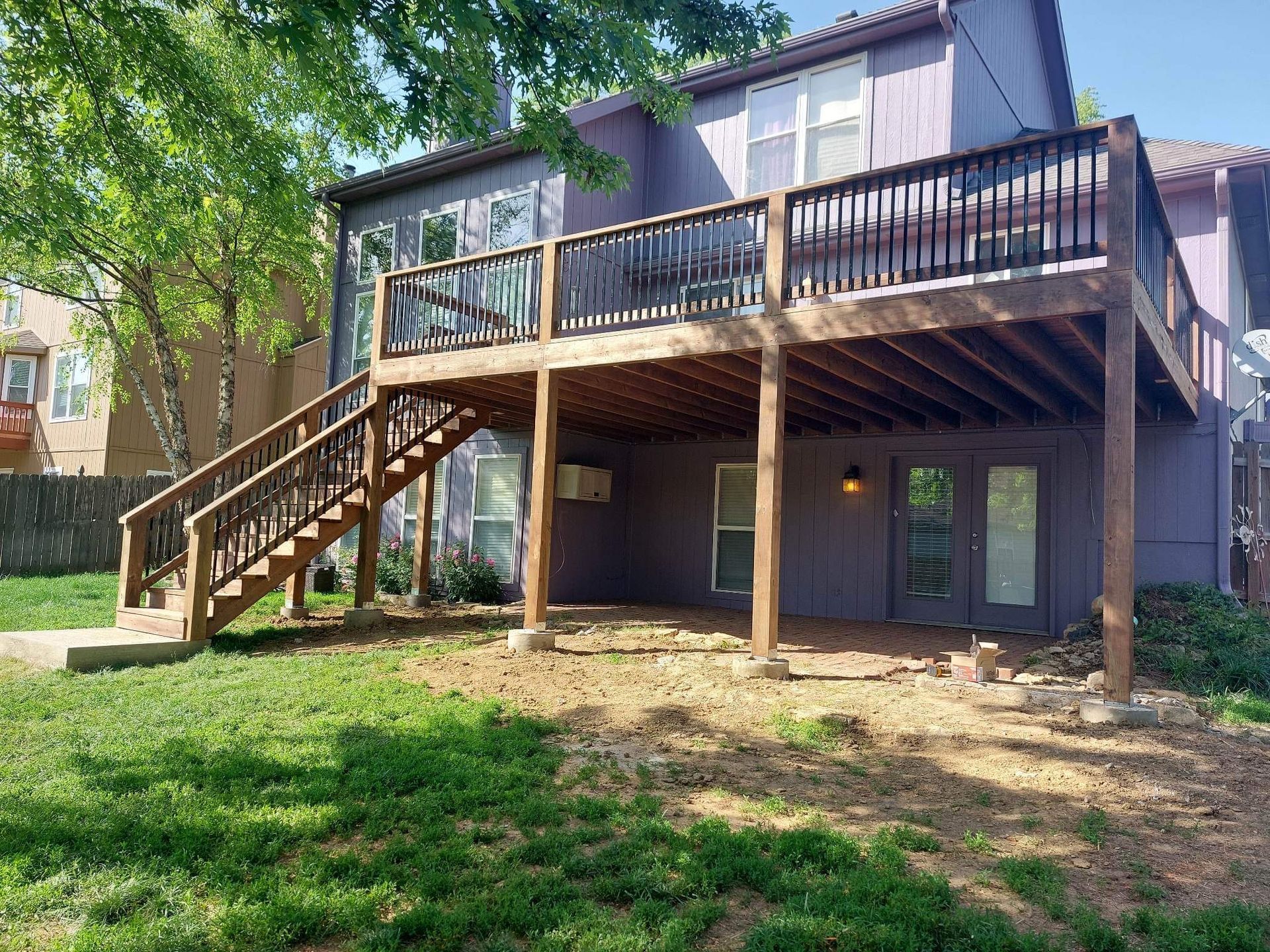 Two-story house with elevated deck and wooden staircase, viewed from a grassy backyard.