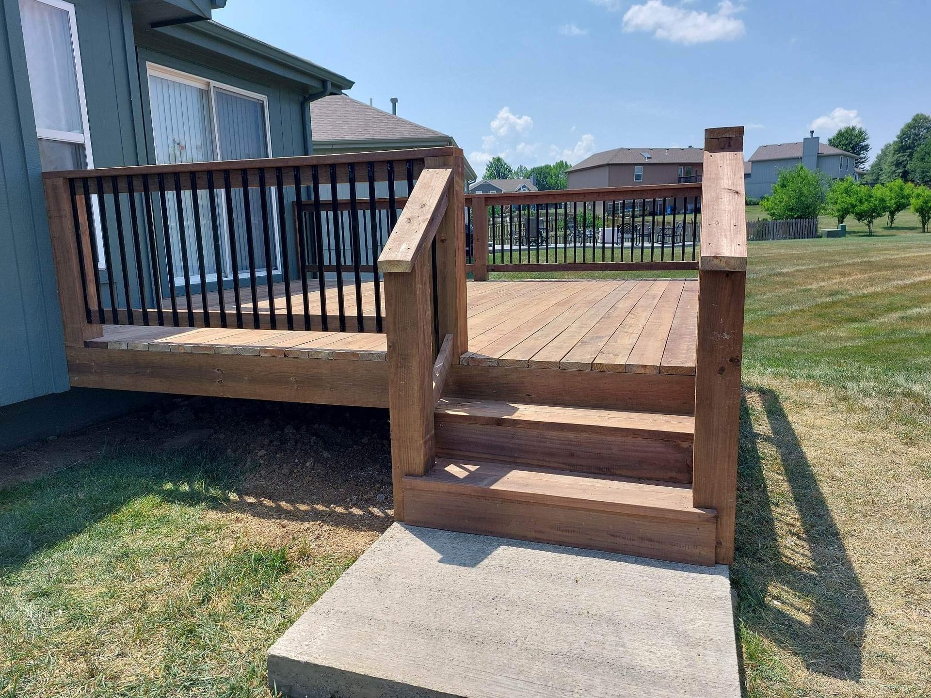 Wooden backyard deck with steps and black railing beside a house on a grassy yard