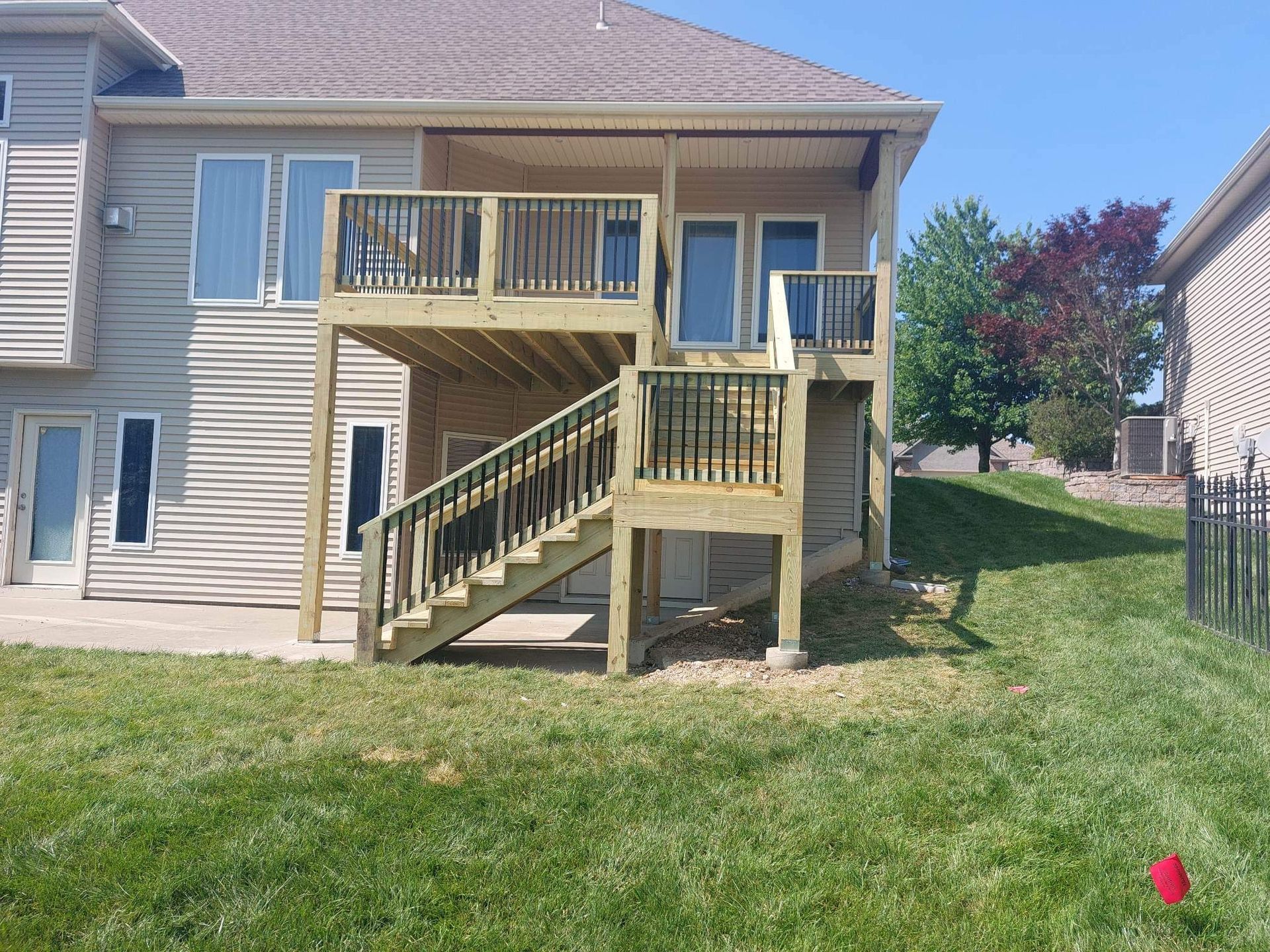 Backyard view of a beige house with a raised wooden deck, stairs, and green lawn