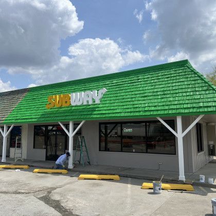 Subway restaurant with a bright green roof and a worker crouching near the entrance
