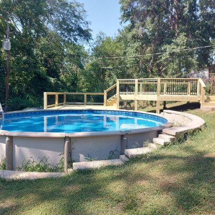 Round above-ground pool in a grassy yard with a small wooden deck and surrounding trees