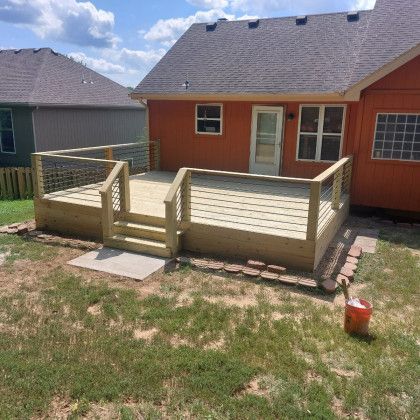 Backyard deck with steps and railing behind an orange house on a sunny day