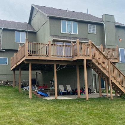 Backyard wooden deck and stairs on a house, with patio furniture underneath and a grassy lawn.
