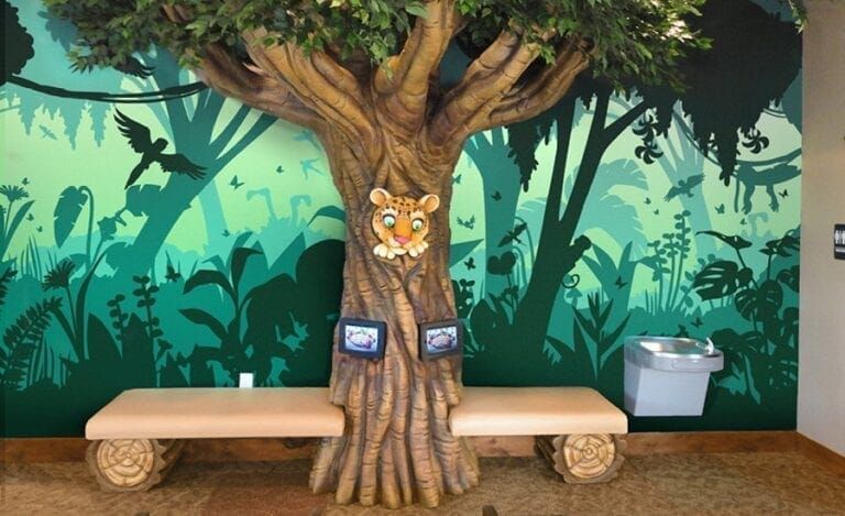 Tree with benches and mural backdrop in a play area. Water fountain and tiger face on the tree.