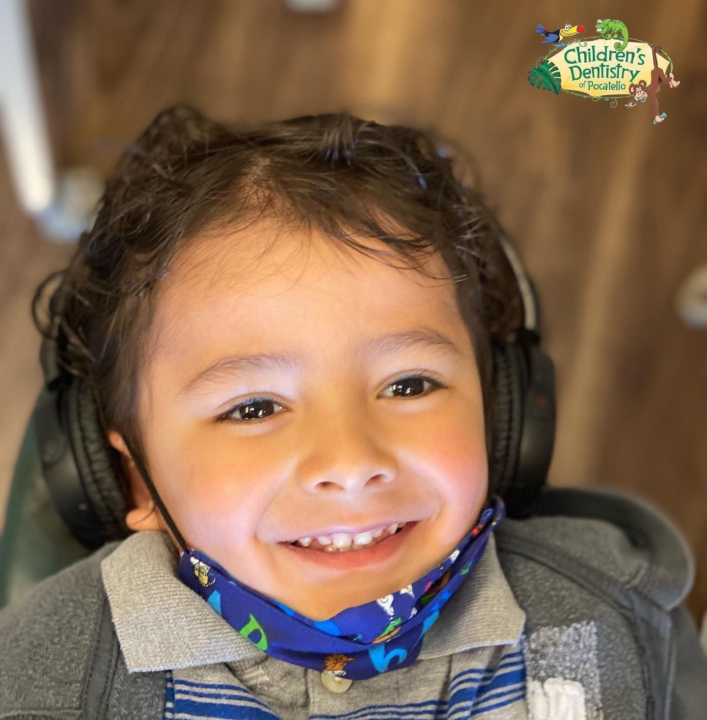 Smiling child wearing headphones and a mask in a dental chair.