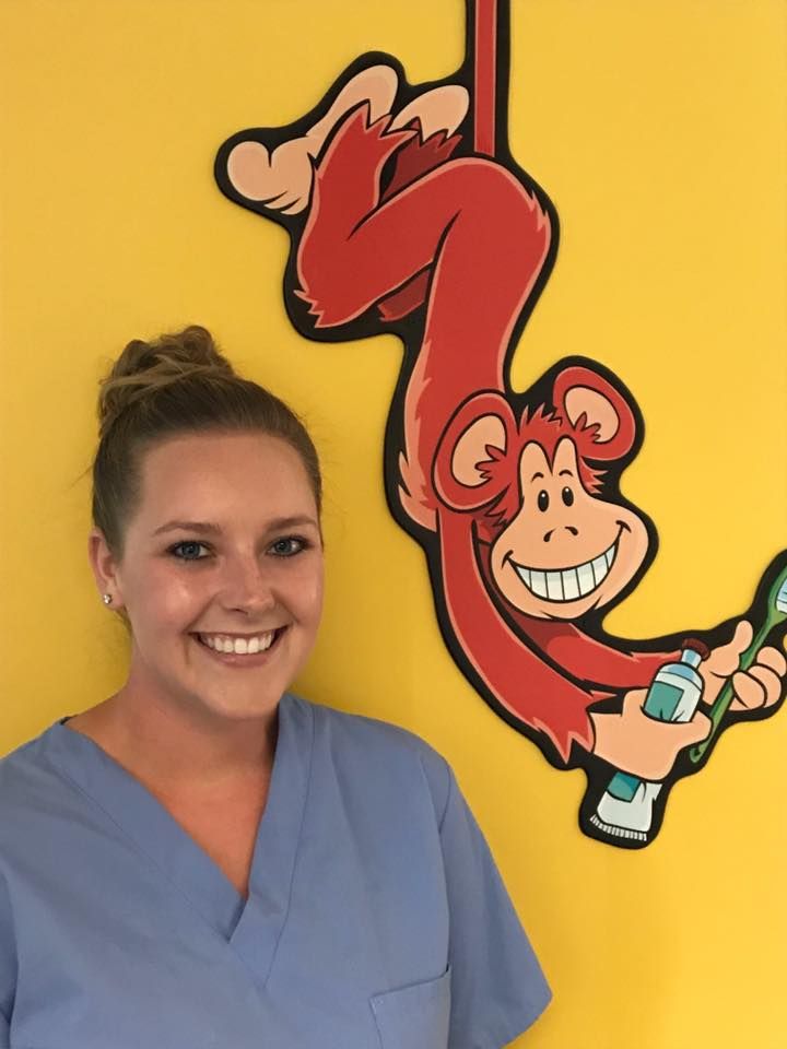 Smiling dental assistant in blue scrubs with monkey wall art.