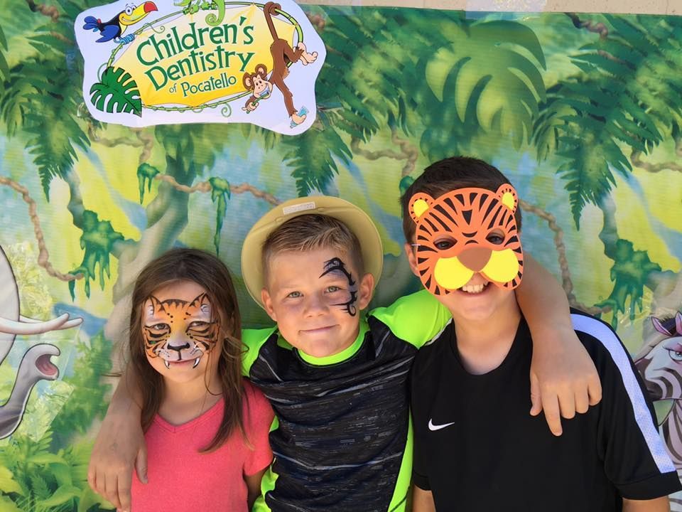 Three children with tiger-themed face paint and masks pose in front of a jungle backdrop at a dentistry event.