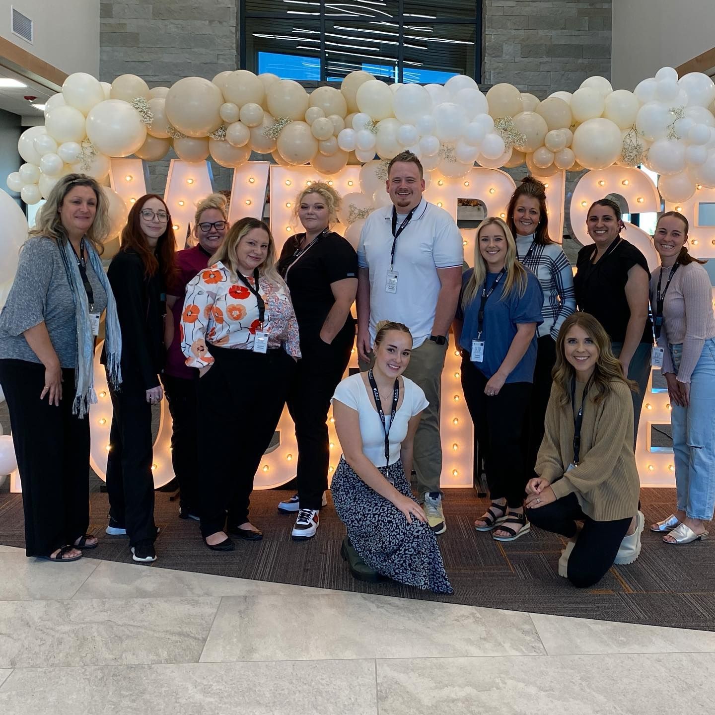 Group of people in front of balloon display with lit up letters. Mostly women, smiling. Indoors.
