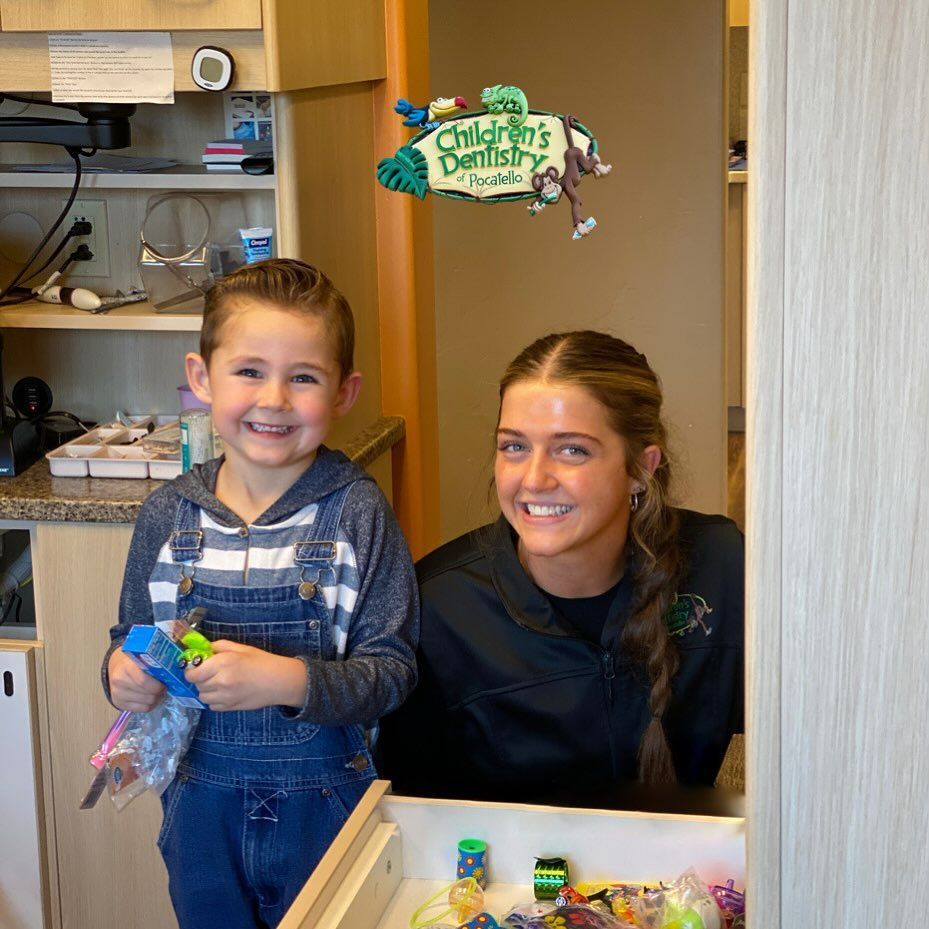 Boy in overalls and staff member smiling at a dentist's office with toys.