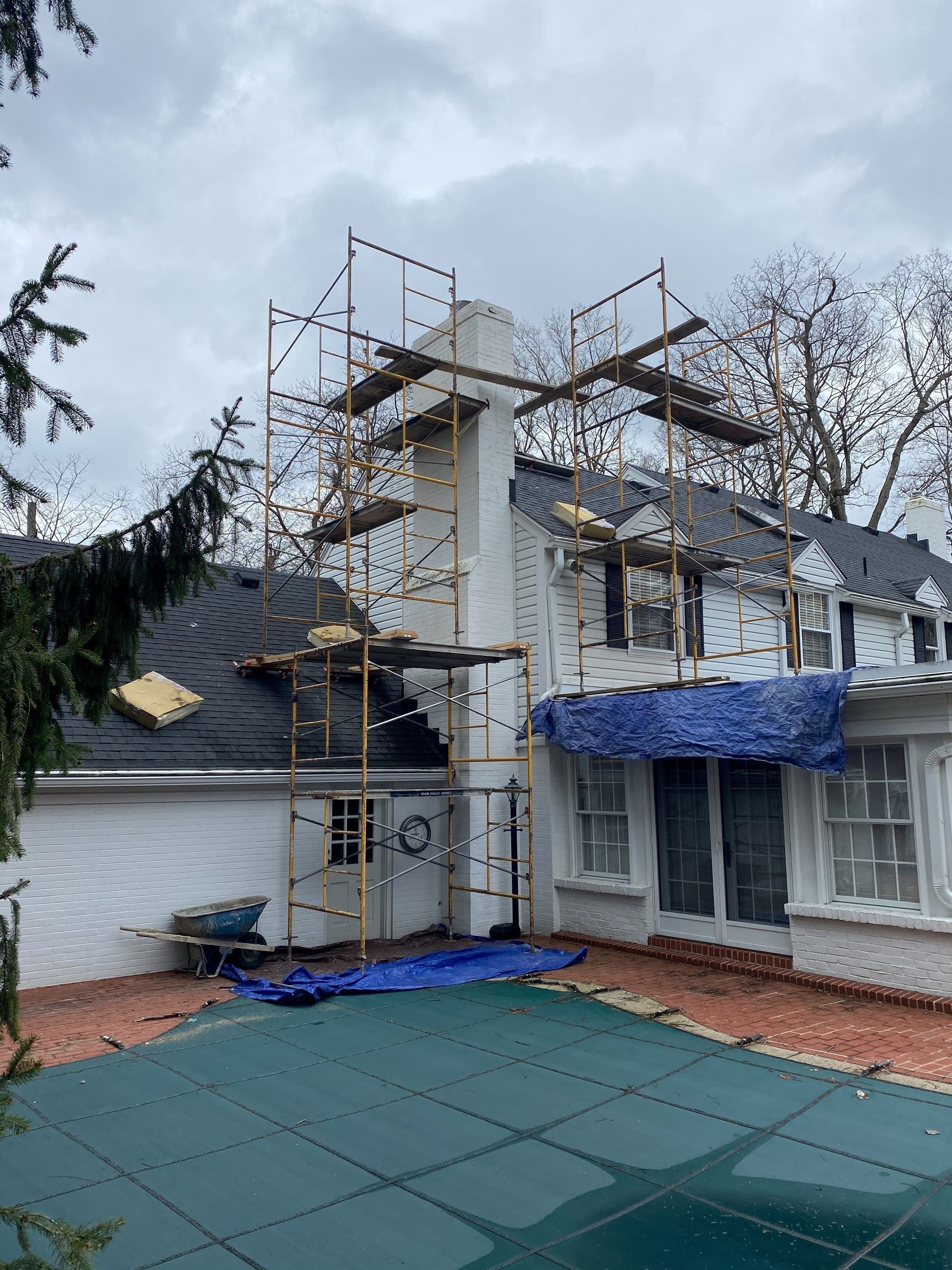 A white house with scaffolding around it and a pool in front of it.