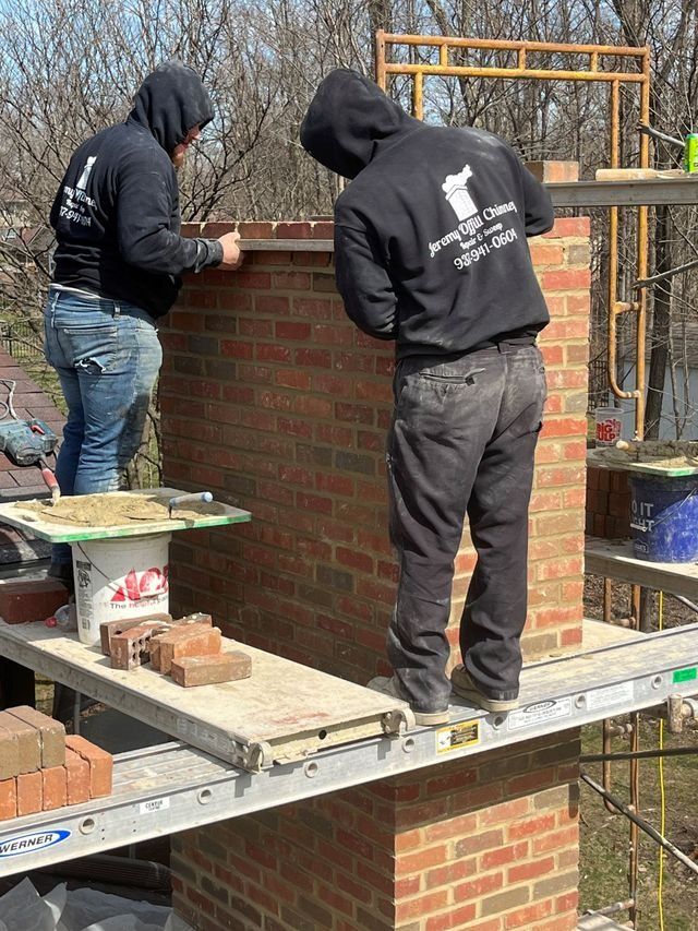 Two men are working on a brick chimney on a scaffolding.