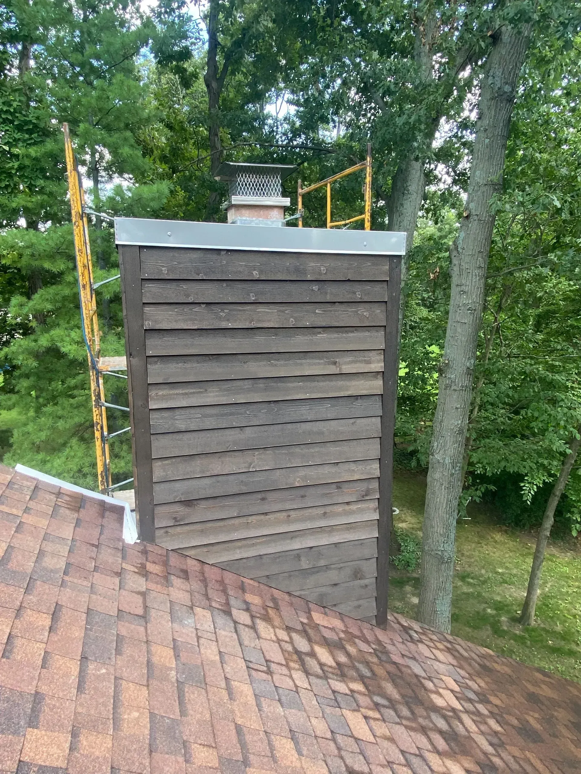 A chimney on top of a roof with trees in the background.